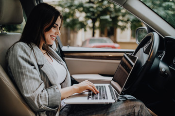 Beautiful young business woman using laptop in the car.