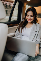 Elegant business woman sitting in car and working on laptop