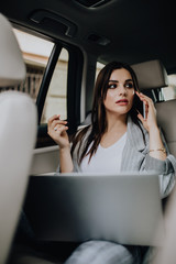 Business woman inside her car using a laptop and a mobile phone