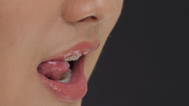 Side shot of young female licking her lips in slow motion. Close up shot of beautiful woman tongue licking her lips with glossy lipstick. close-up of lips.
