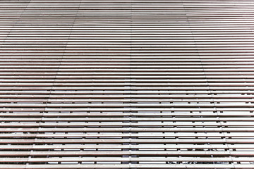 Facade of the modern building made of multiple timber battens in parallel; the striped wooden facade of a contemporary house with windows behind