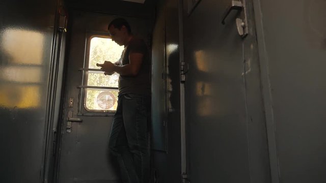 the man silhouette is standing on the train Railway carriage holding a smartphone and . slow motion video. man writes messages in the smartphone in the train social media. man lifestyle with