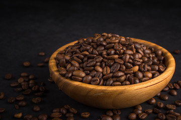Fresh fried coffee beans in a wooden bowl on a black stone background.