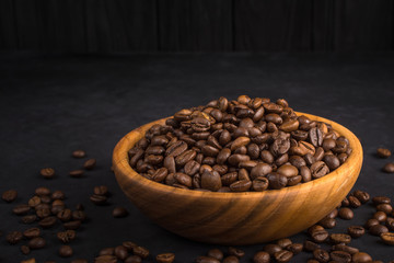 Fresh fried coffee beans in a wooden bowl on a black stone background with space for your text.