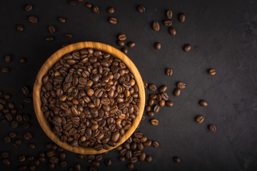 Fresh roasted coffee beans in a wooden bowl on a black stone background top view with space for your text.
