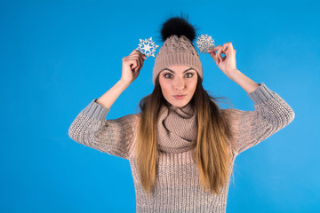 The girl is dressed in a knitted warm sweater and hat. Young woman holding two shiny snowflakes