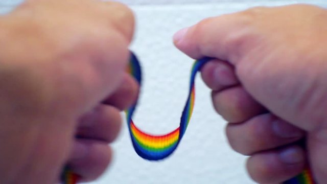 male hands stretch ribbon painted in LGBT colors on a light background.Closeup
