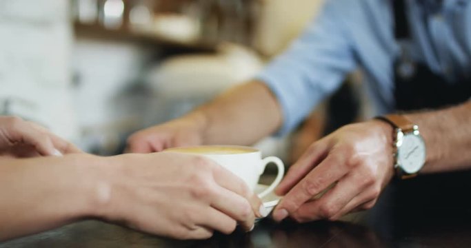 Close upof the cup of coffee being given from man's hands of barmen to the female client at the cafe.