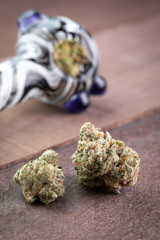 Cannabis buds on wood, with a packed marijuana pipe in the background
