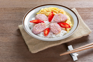 close up of rice vermicelli with fermented pork sausage and omelette in a ceramic dish on wooden table. asian homemade style food concept.