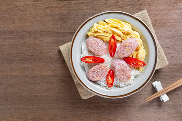 top view of rice vermicelli with fermented pork sausage and omelette in a ceramic dish on wooden table. asian homemade style food concept.
