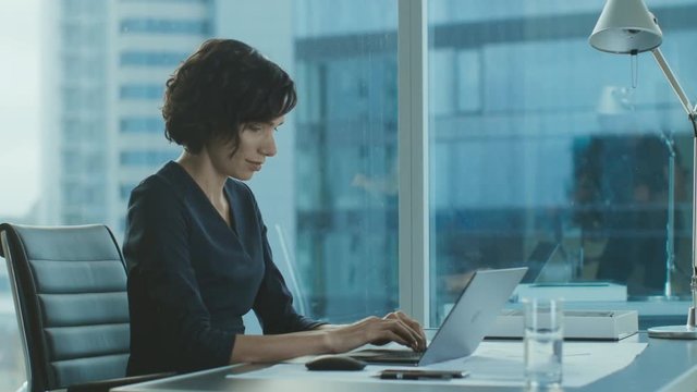 Side View Portrait of the Beautiful Businesswoman Working on a Laptop in Her Modern Office with Cityscape Window View. Female Executive Uses Computer.