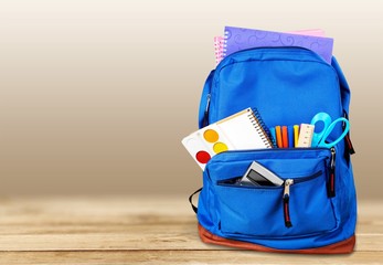 Open blue school backpack on wooden table in classroom