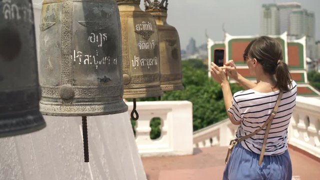 Woman taking photo with cellphone of bells in Buddhist temple
