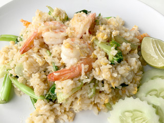 Fried rice with prawn herbs and vegetables served with lemon and cucumber in white plate on white background. Part of a series of nine Asian food dishes. Thai Food.