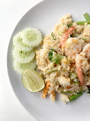Fried rice with prawn herbs and vegetables served with lemon and cucumber in white plate on white background. Part of a series of nine Asian food dishes. Thai Food.