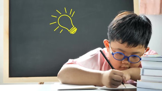 Cute little boy asian with a bright idea light bulb above his head while writing into book. concept for innovation, imagination and inspirational ideas..