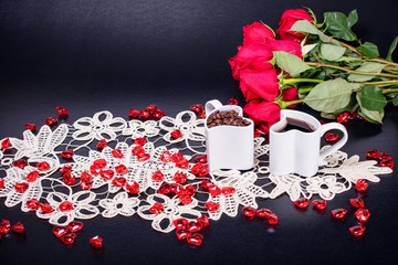 Hearshaped coffee mugs on a black background with text space.  Red roses and red glass hearts scattered on a lace tablecloth
