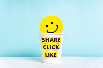 Social media and content marketing concept with happy smiling yellow face over cup paper and share click like words, blue background.