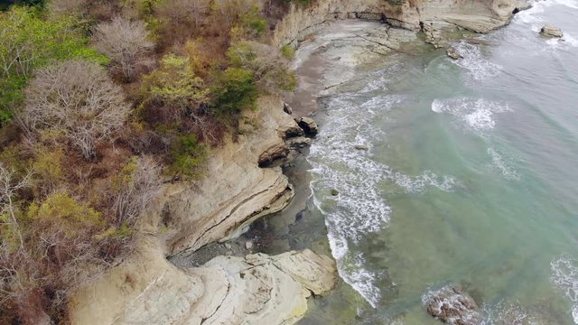 Aerial shot of an undeveloped tropical beach "Playa Escondida" in Esmeraldas province, Ecuador, with exposed mudstone pavement and cliffs, tropical dry forest growing on clifftops.