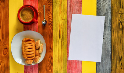 puff pastry with jam on a red plate and coffee mug on a multi-colored wooden background