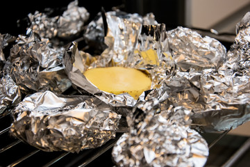 Halved potatoes wrapped in aluminum foil, lying on the grate of the oven.