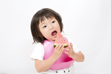 白バックでスイカを手に持ち食べている幼い女の子、子供の健康、成長,育児、おやつイメージ