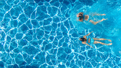 Aerial drone view of children in swimming pool from above, happy kids swim on inflatable ring donuts, girls have fun in water on family vacation
