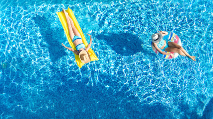 Aerial drone view of children in swimming pool from above, happy kids swim on inflatable ring donuts, girls have fun in water on family vacation
