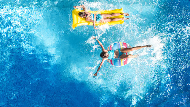 Aerial drone view of children in swimming pool from above, happy kids swim on inflatable ring donuts, girls have fun in water on family vacation
