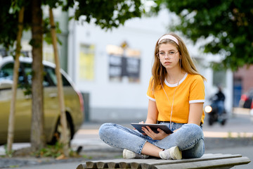 Young girl student with tablet listening to music in city with traffic