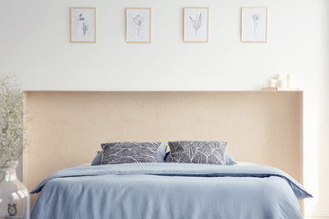 Patterned pillows on blue bed in minimal white bedroom interior with posters and plant. Real photo
