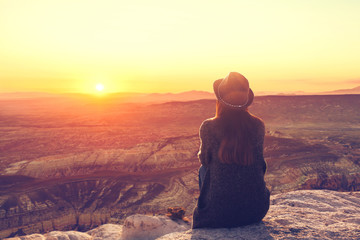 A girl in a hat on top of a hill in silence and loneliness admires a tranquil natural landscape in...