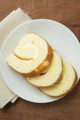 Slices of vanilla roll cake in white plate on wooden table.