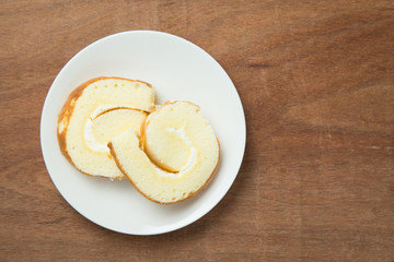 Slices of vanilla roll cake in white plate on wooden table.