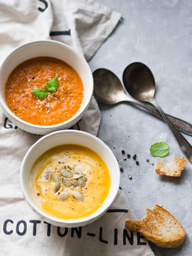 Homemade autumn soups -  pumpkin cream-soup and tomato cream soup on a linen towel on a gray background
