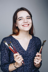Close up studio portrait of happy smiling artist girl holding paintbrushes isolated on grey background. Paint brush tools. Art concept