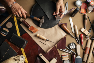 Top view of male shoemaker hands holding cobbler tools for making new shoes at his workshop over his working place background - obrazy, fototapety, plakaty
