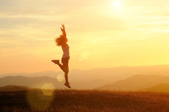Happy woman with open arms jumping on the peak of the mountain beautiful sunset background