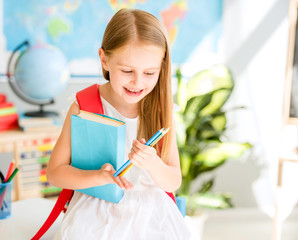 Little smiling blond girl standing in the school classroom