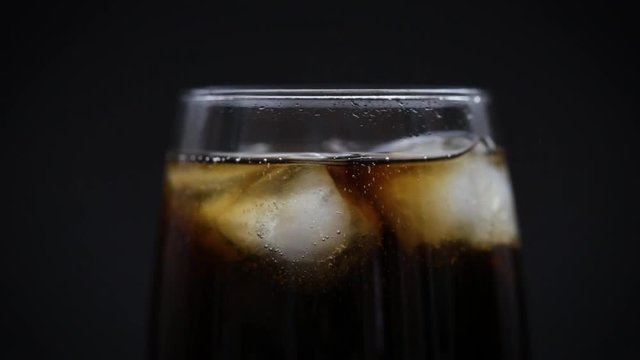 Cola in a glass with ice on a black background closeup