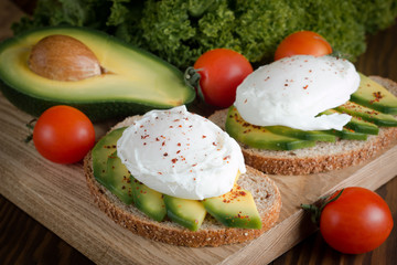 Avocado toast, cherry tomato and poached eggs on wooden background. Breakfast with vegetarian food, healthy diet concept.