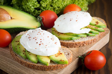 Avocado toast, cherry tomato and poached eggs on wooden background. Breakfast with vegetarian food, healthy diet concept.