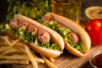 Photo of barbecue grilled hot dog with yellow mustard and ketchup on wooden background. Hot dog sandwich with potato fries and sauces.