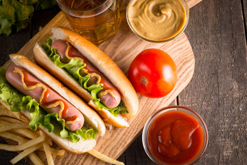 Photo of barbecue grilled hot dog with yellow mustard and ketchup on wooden background. Hot dog sandwich with potato fries and sauces.