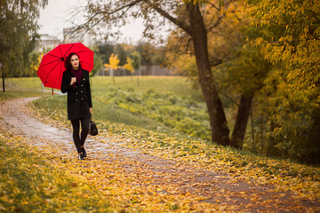 a girl walks in the autumn park under an umbrella
