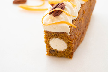 Carrot cake pie, sprinkled with nuts, decorated with cream-colored carrots on white marble.