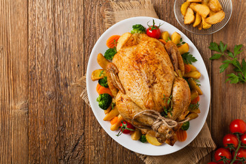 Roast chicken whole. Served on a plate with vegetables and baked potatoes.