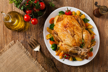 Roast chicken whole. Served on a plate with vegetables and baked potatoes.
