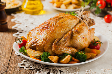 Roast chicken whole. Served on a plate with vegetables and baked potatoes.